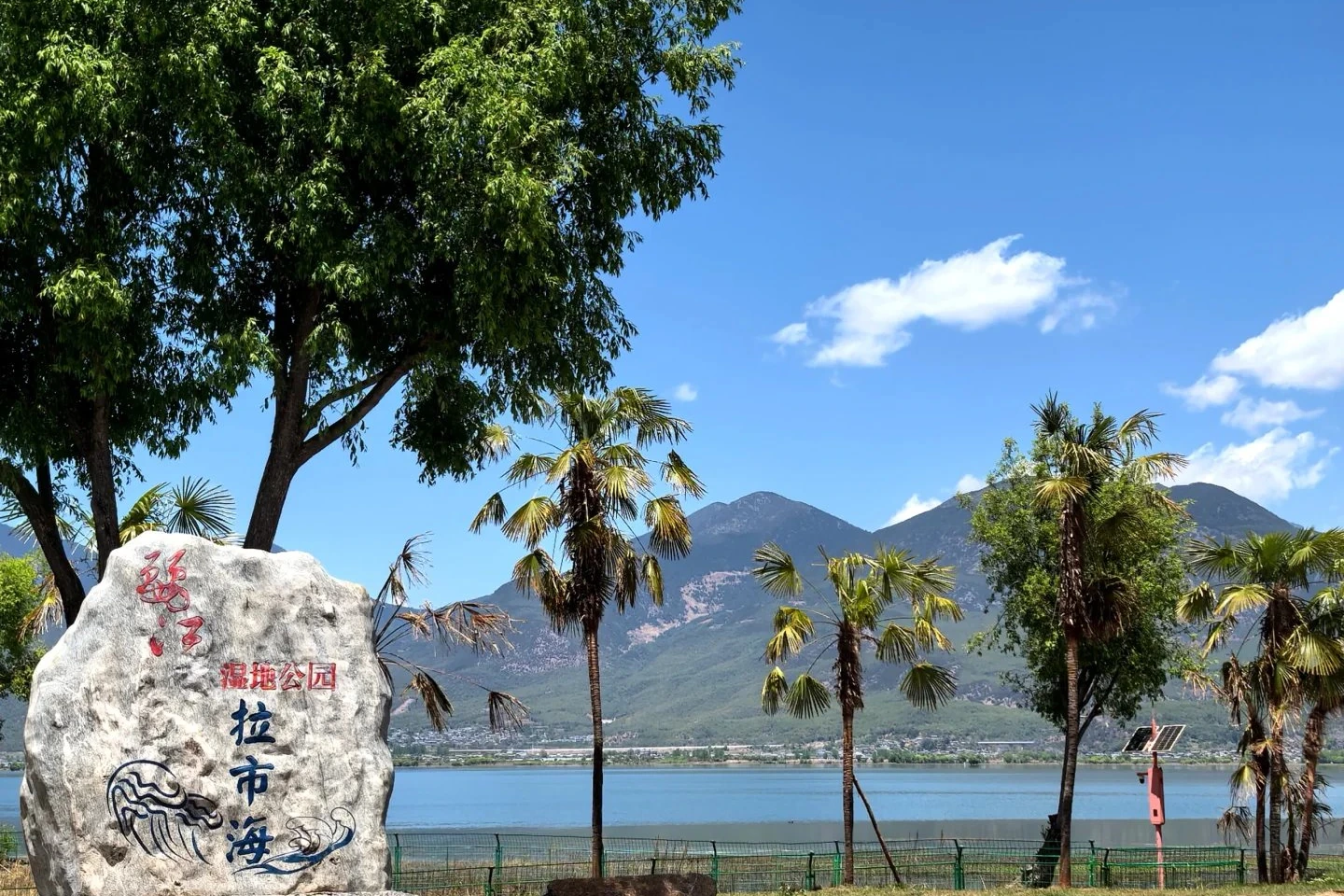 Lashi Lake wetland park entrance stone with palm trees and mountains beyond the water