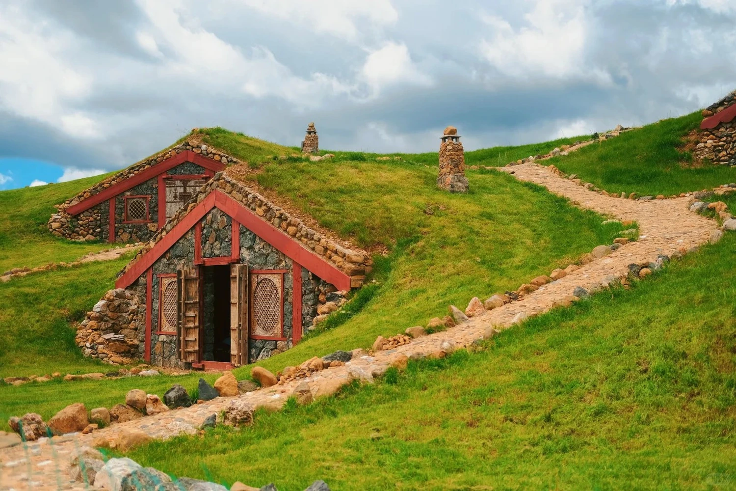 Yuhu Village stone cottage with turf roof and stone path under green meadow and sky