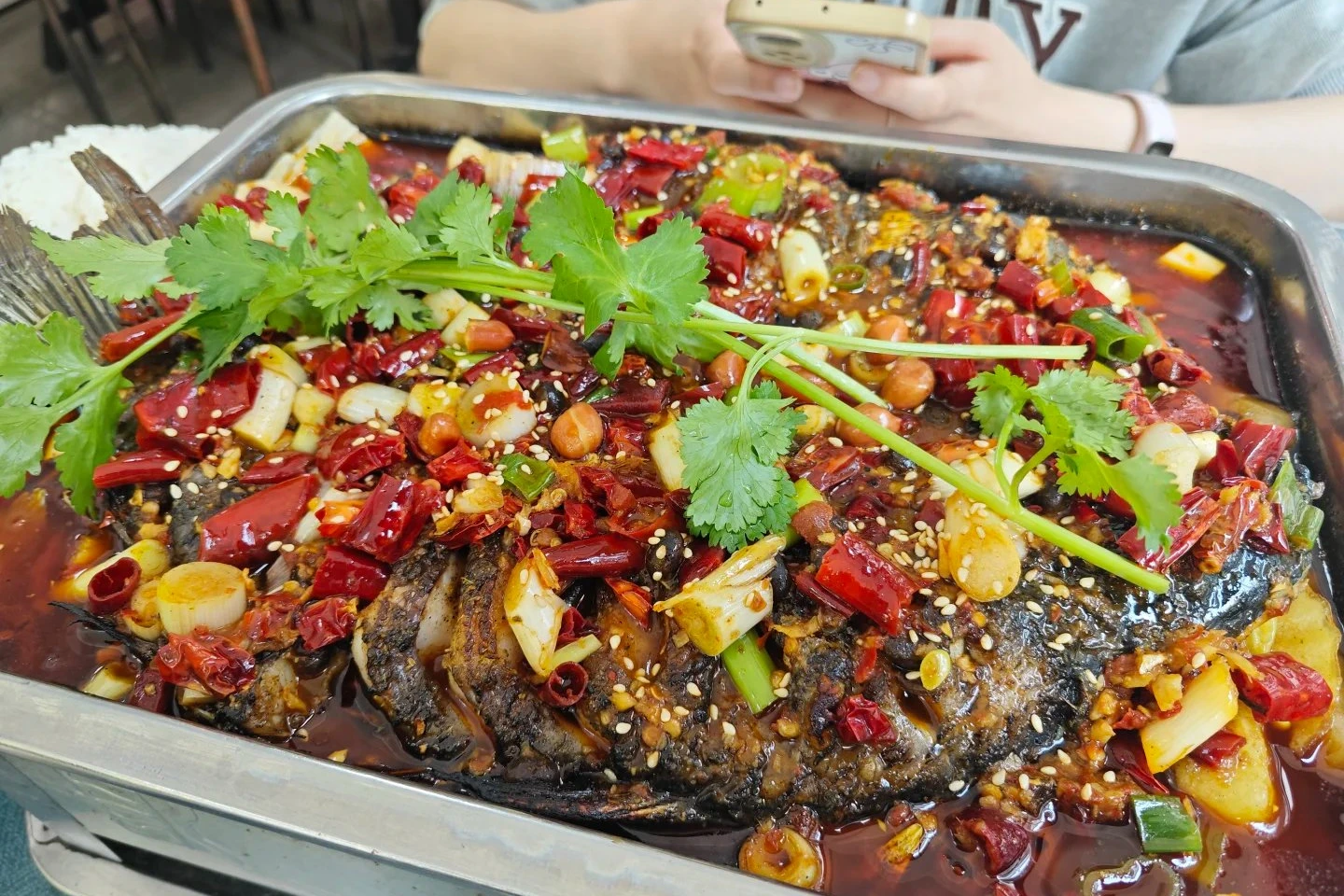 Naxi grilled fish topped with red chilies, garlic, peanuts, and sesame seeds on metal tray
