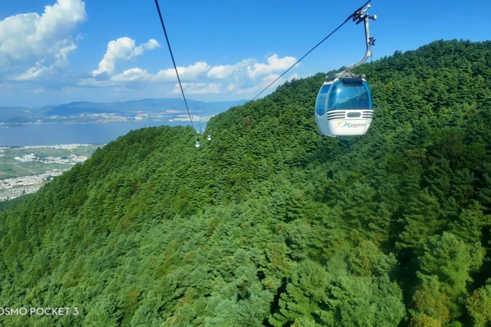 Gantong cable car cabin suspended above lush green forest with Dali city and Erhai Lake visible below